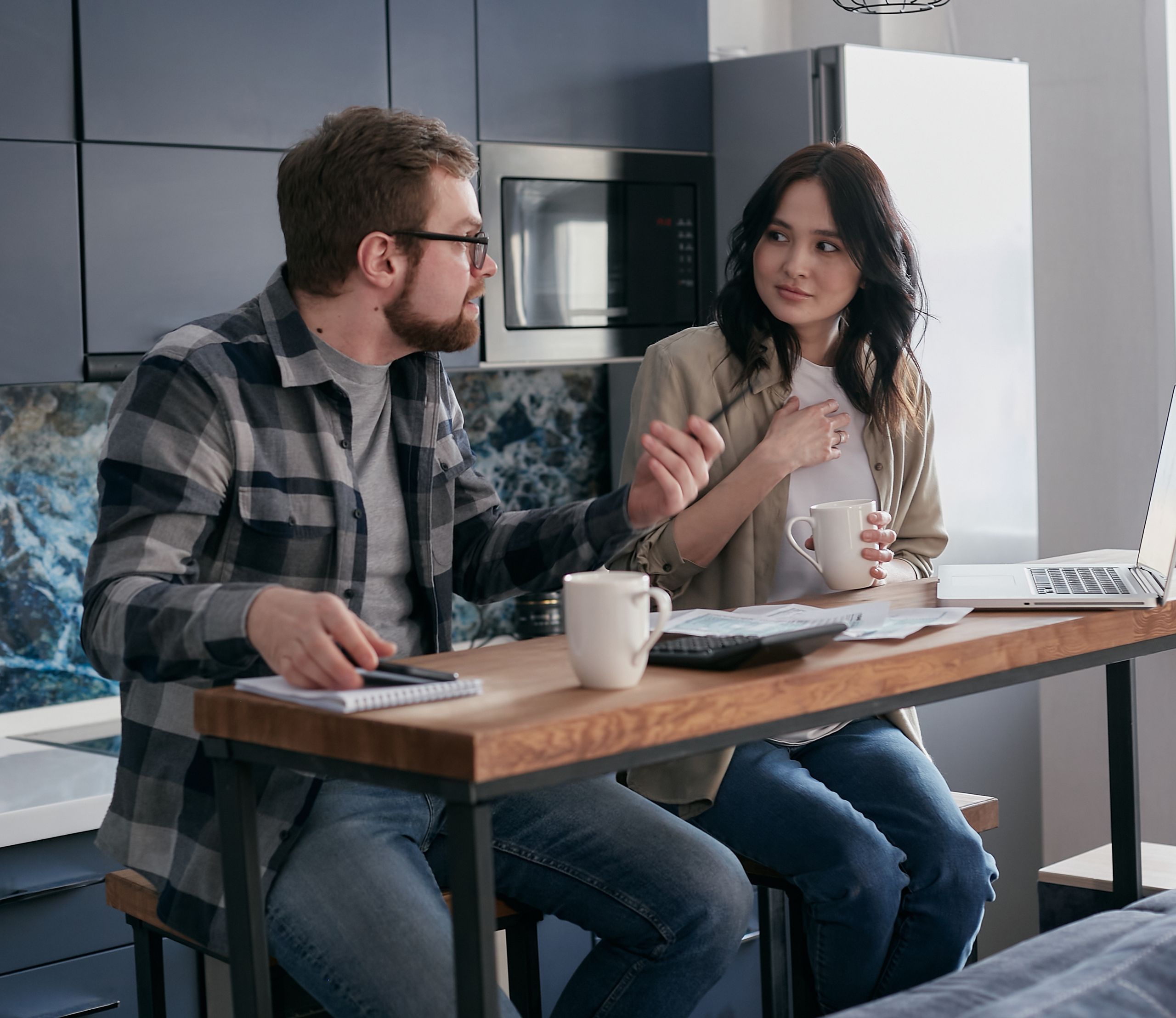Two adults discussing ideas in a modern kitchen setting with coffee and a laptop.